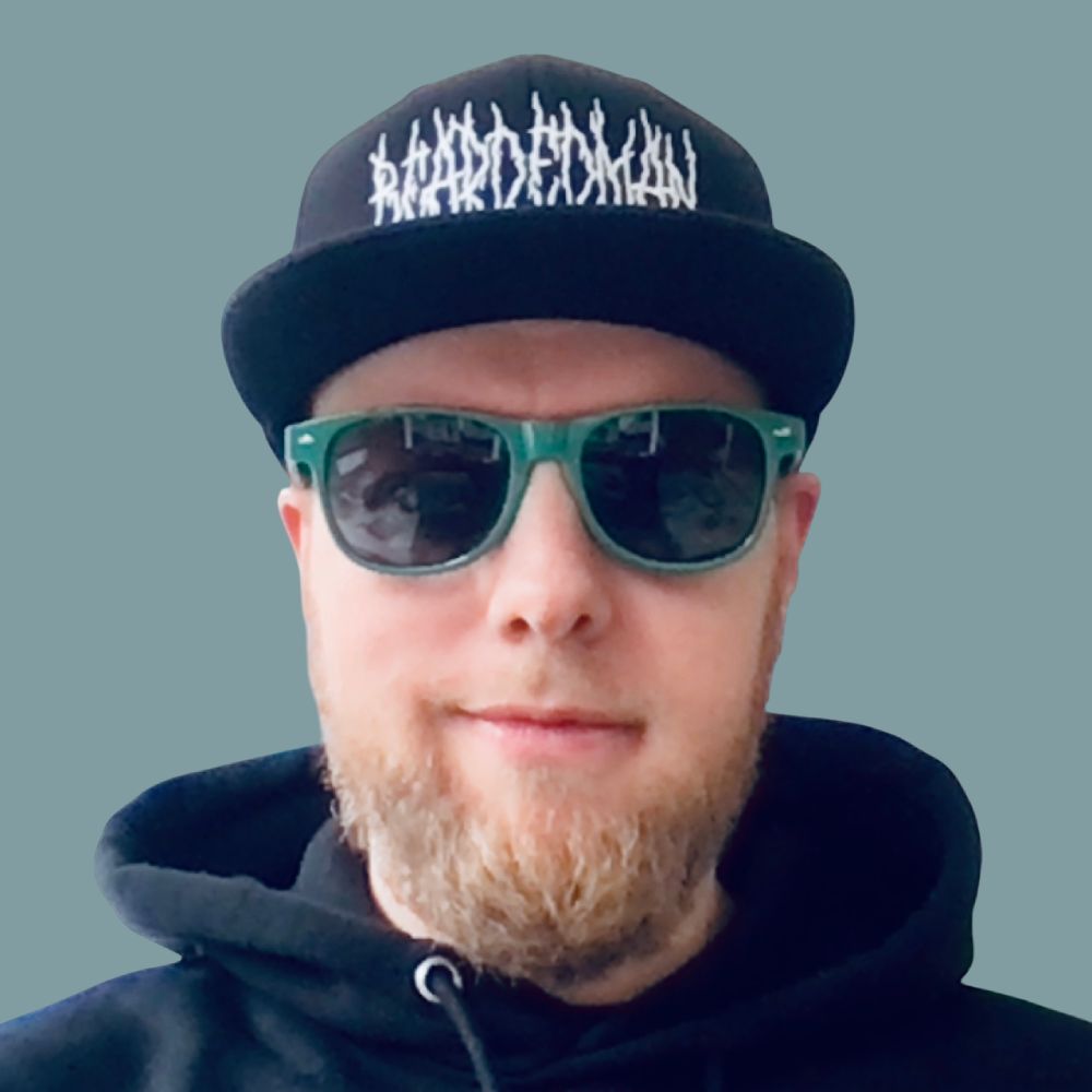 Photo of me wearing green sunglasses and a black hat that says beadbearded man.